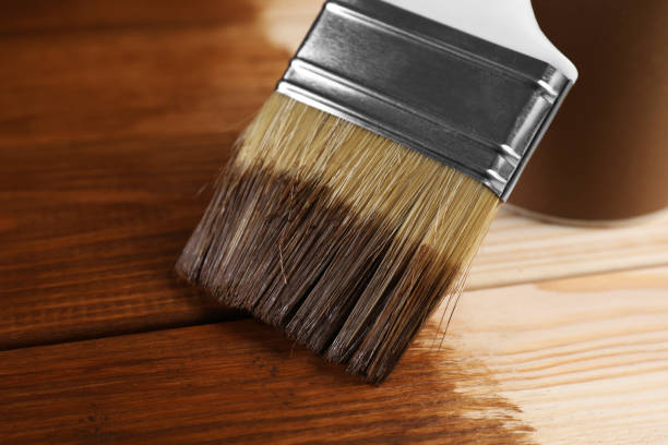 Wood staining brush applying a rich finish to natural wood, illustrating professional wood staining by a painting company in Sunapee, NH.